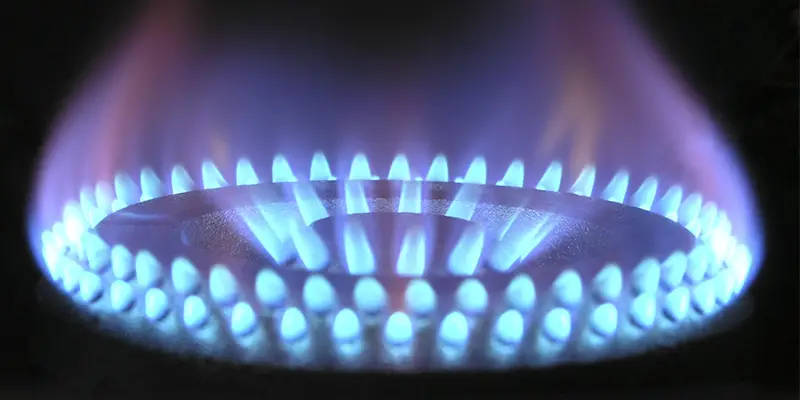 A close up of a blue gas flame on a cooker ring against a black background