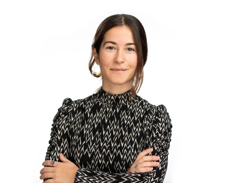 Veronica Frincu from Innovate UK KTN wearing big hoop earrings and a black high-necked and long-sleeved top with white zig zags. She has her arms crossed and her long black hair tied up