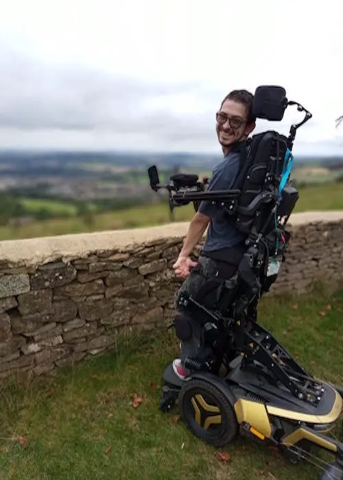 Nath smiling in his wheelchair looking out over a stonewall at fields