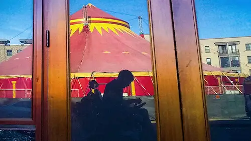 A man in a wheelchiar in the shadows against a background of a circus tent.